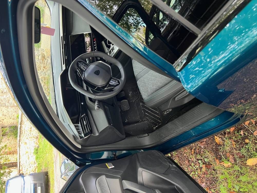Porte de voiture ouverte laissant apparaître un volant noir et un tableau de bord dans un véhicule bleu sarcelle.