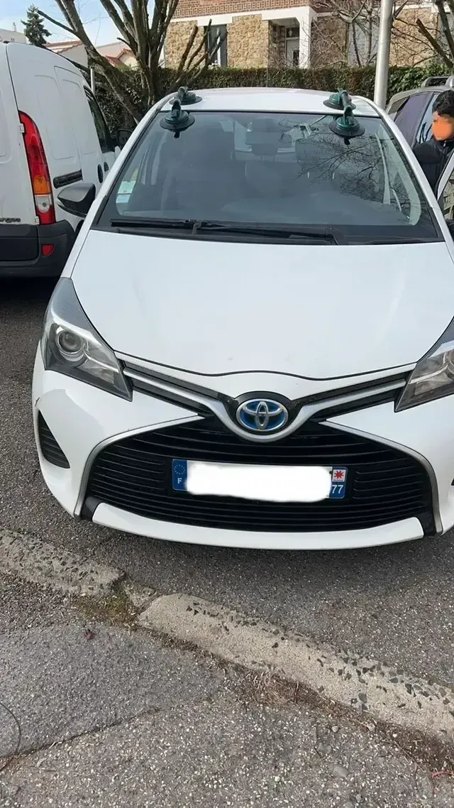 Voiture Toyota blanche garée dans une rue étroite, à côté d’une camionnette blanche et d’arbres