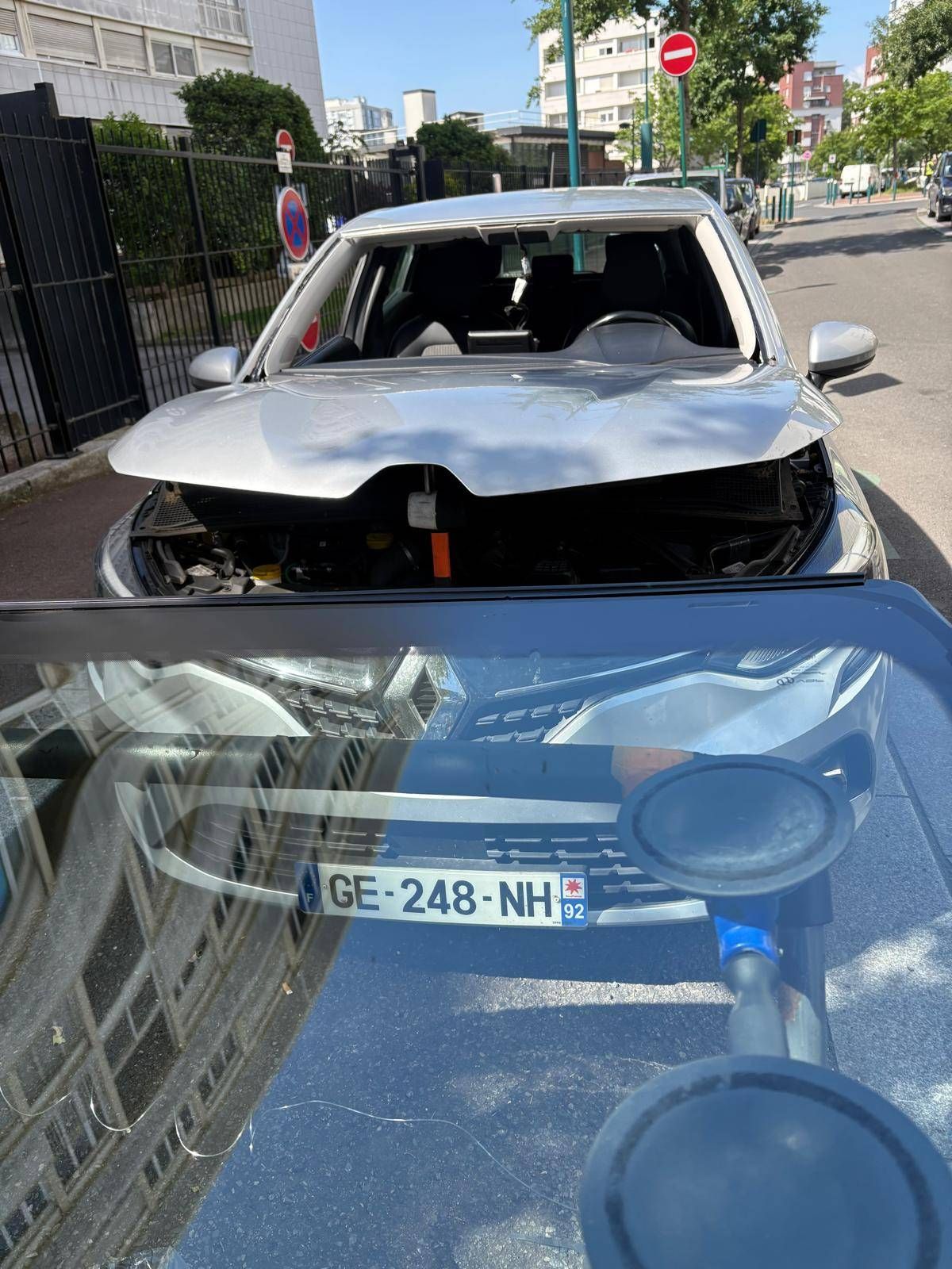 Voiture argentée lourdement endommagée, avec le pare-brise brisé et le capot enfoncé, dans une rue de la ville