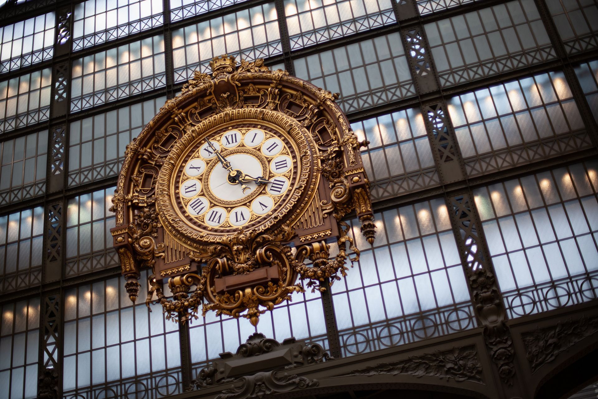 Un reloj dorado adornado cuelga en un edificio con techo de cristal.