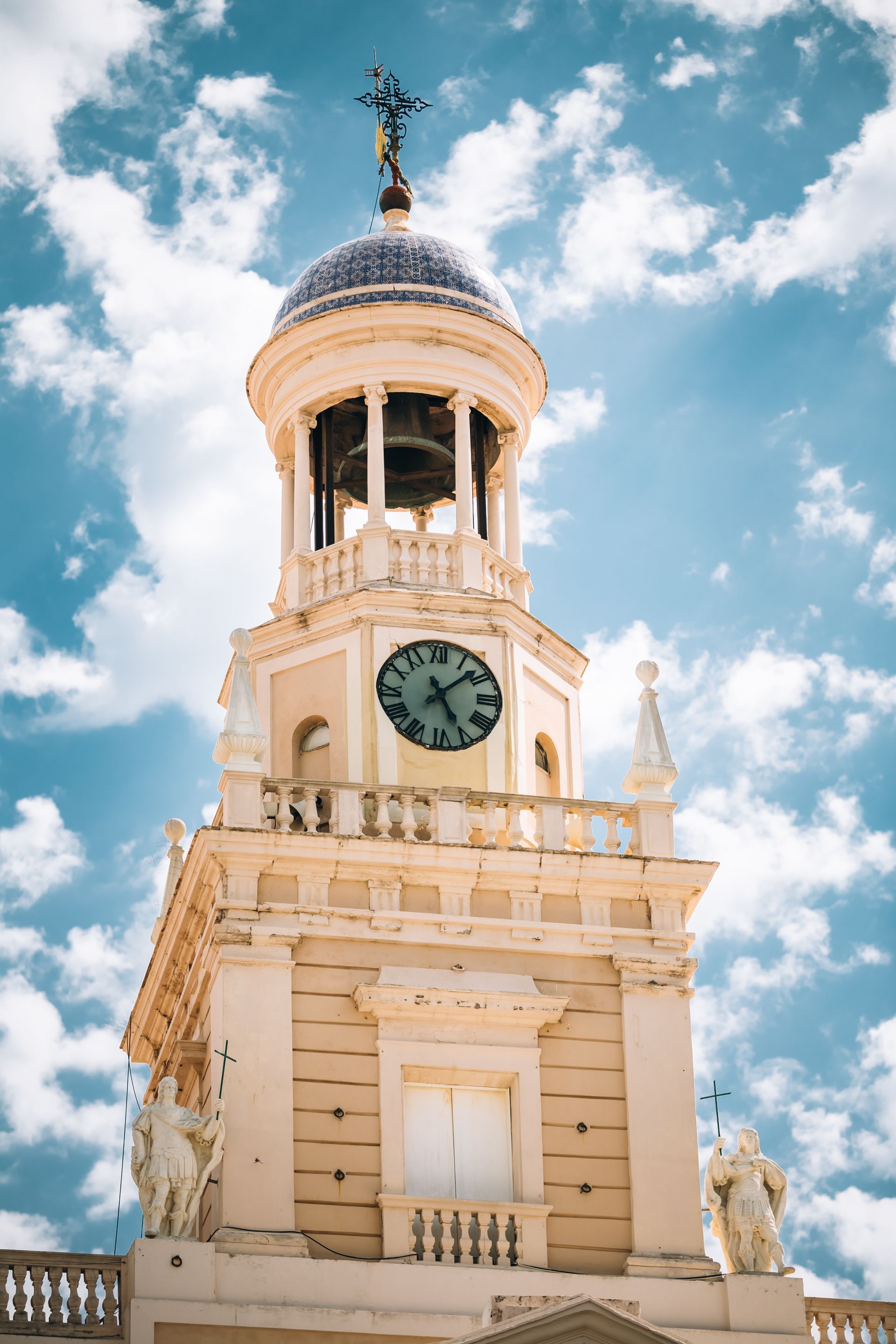 Torre del reloj con detalles ornamentados, esfera del reloj y cúpula contra un cielo parcialmente nublado.