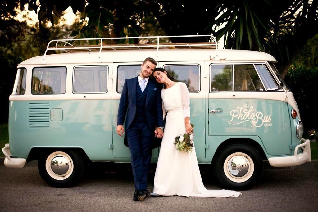 Los recién casados ​​posan junto a una furgoneta VW vintage en tonos verde azulado y blanco. El hombre con traje y la mujer con vestido de novia.