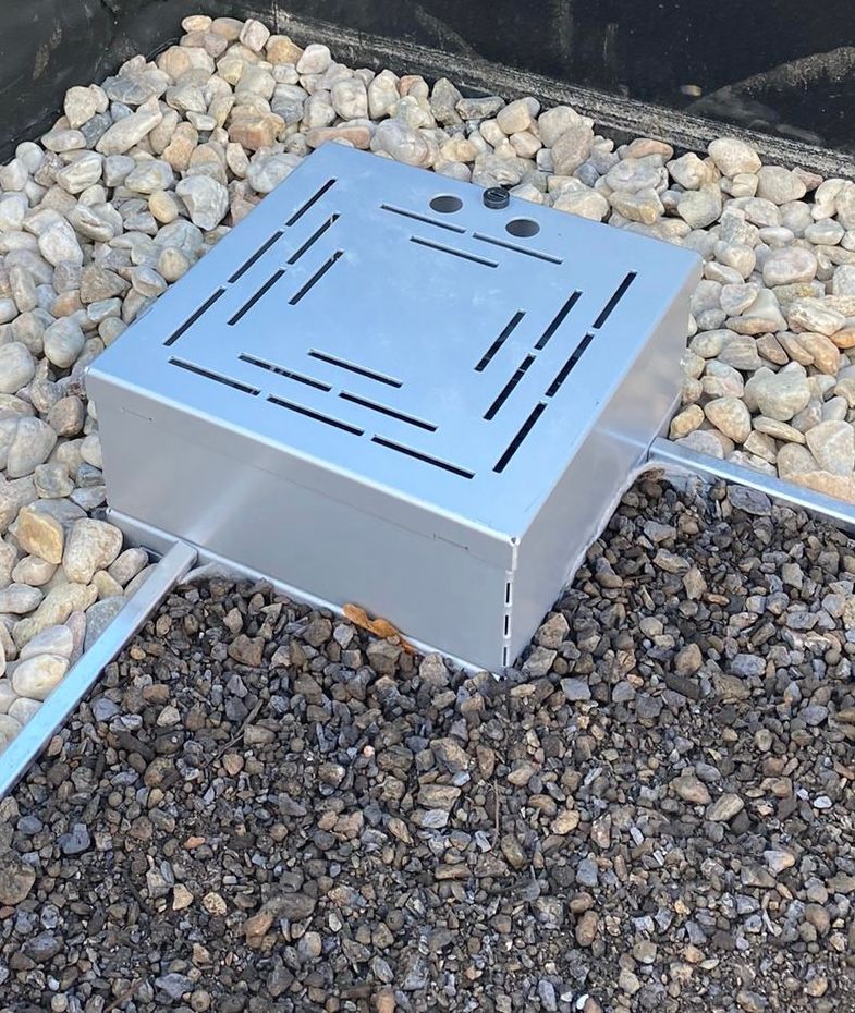 Quadratischer Kontrollschacht aus Metall auf einem mit Kies aufgeschütteten Flachdach.
