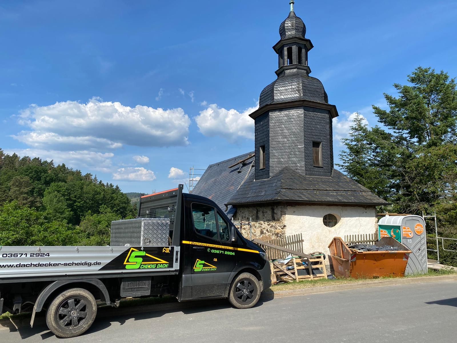 Dachdecker-LKW vor einer kleinen Schieferkapelle an einer Baustelle.