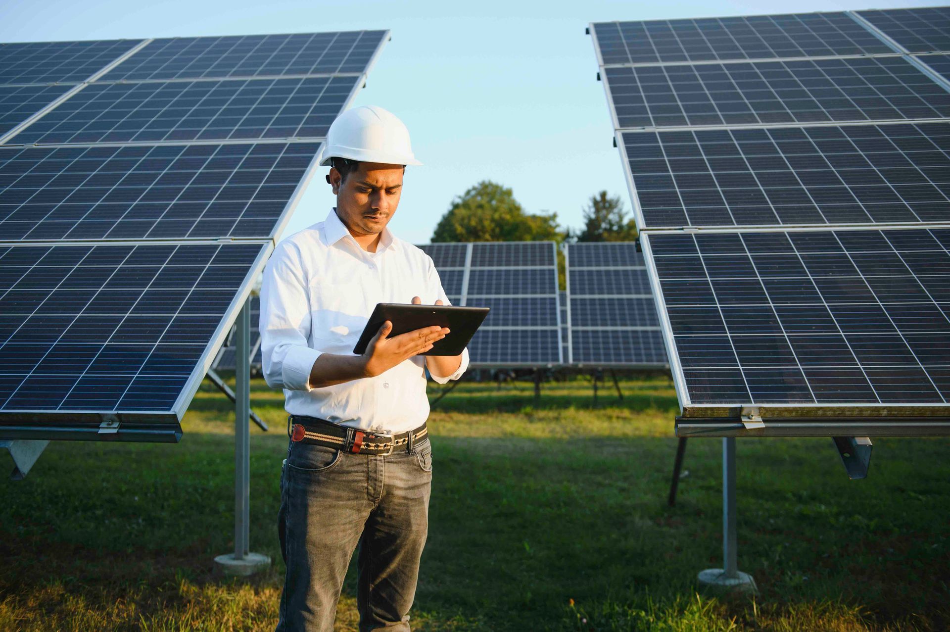Ein Mann steht vor einem Solarpanel und schaut auf ein Tablet.