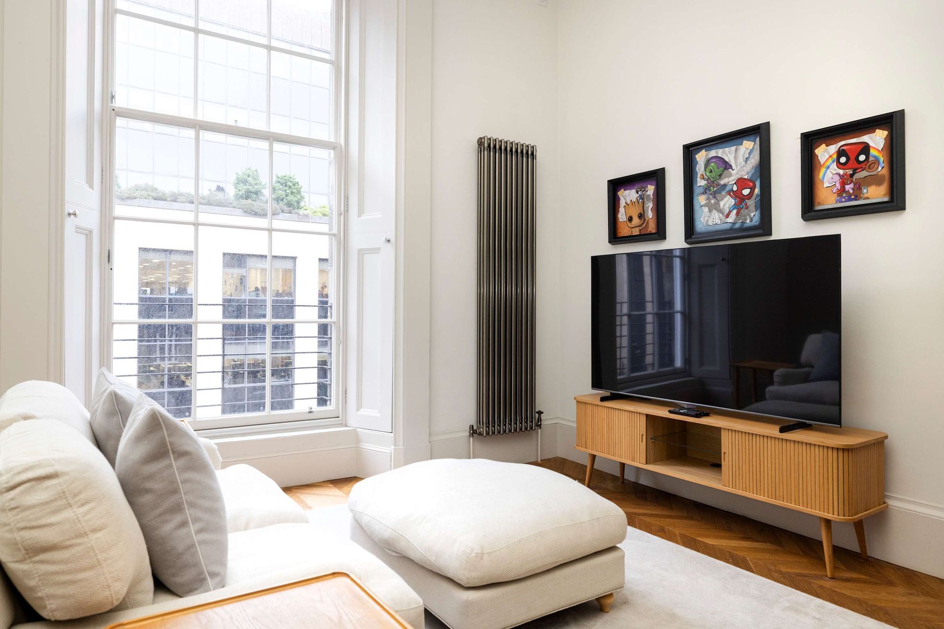 A living room with a couch , ottoman , television , and window.