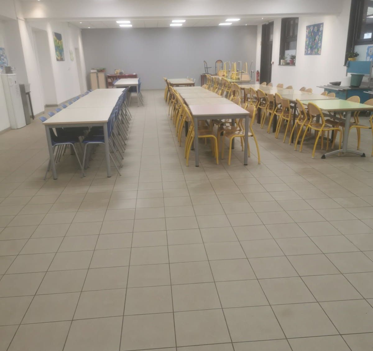 Salle de cantine scolaire avec plusieurs tables longues et chaises