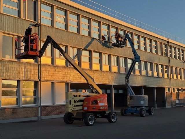 Deux ouvriers, à bord de nacelles élévatrices, effectuent des travaux d'entretien sur la façade d'un immeuble de plusieurs étages.