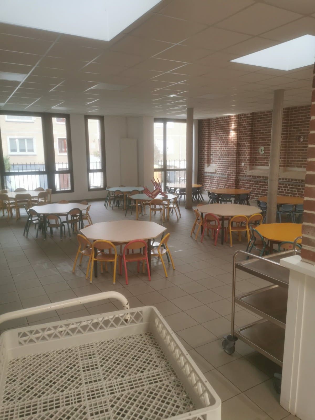 Plusieurs tables rondes entourées de chaises dans une cantine scolaire
