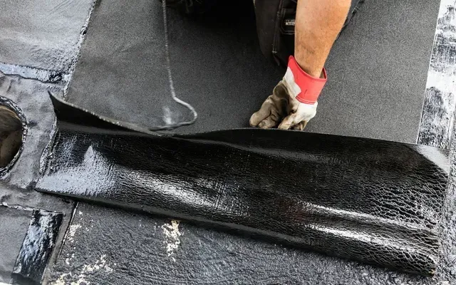 Un trabajador extiende una membrana impermeabilizante negra sobre un tejado plano.