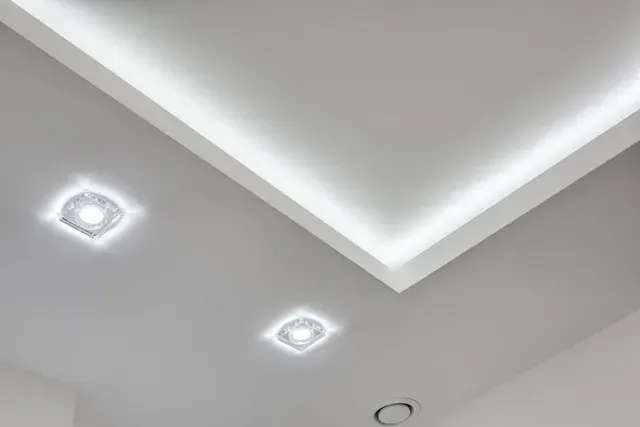 Esquina de techo blanca con iluminación LED empotrada y dos luces de techo cuadradas.