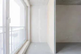 Apartamento luminoso y vacío con grandes ventanales y barandilla en el balcón, que muestra un interior minimalista.
