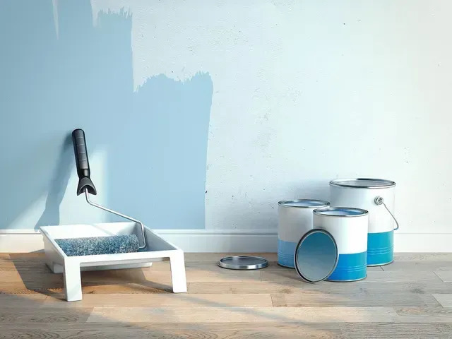 Un rodillo de pintura, una bandeja y latas de pintura azul están sobre el suelo junto a una pared.
