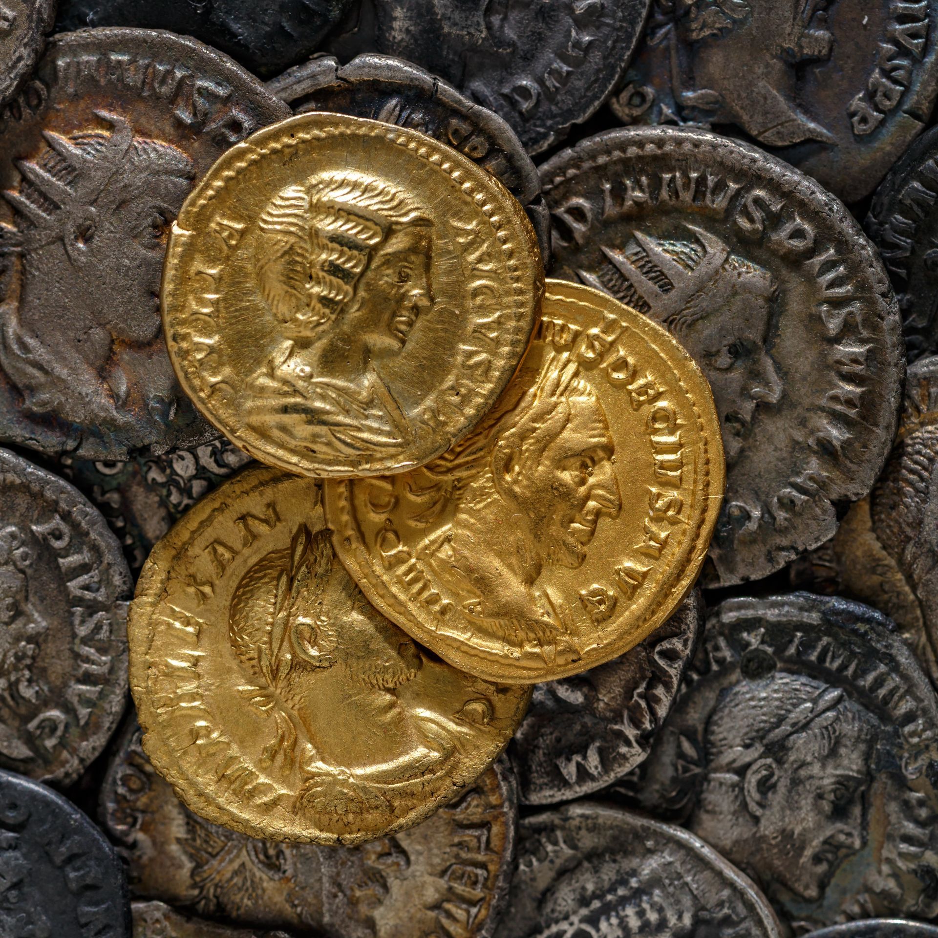 Pièces d'or sur une pile de pièces d'argent ; visages de profil sur les pièces.