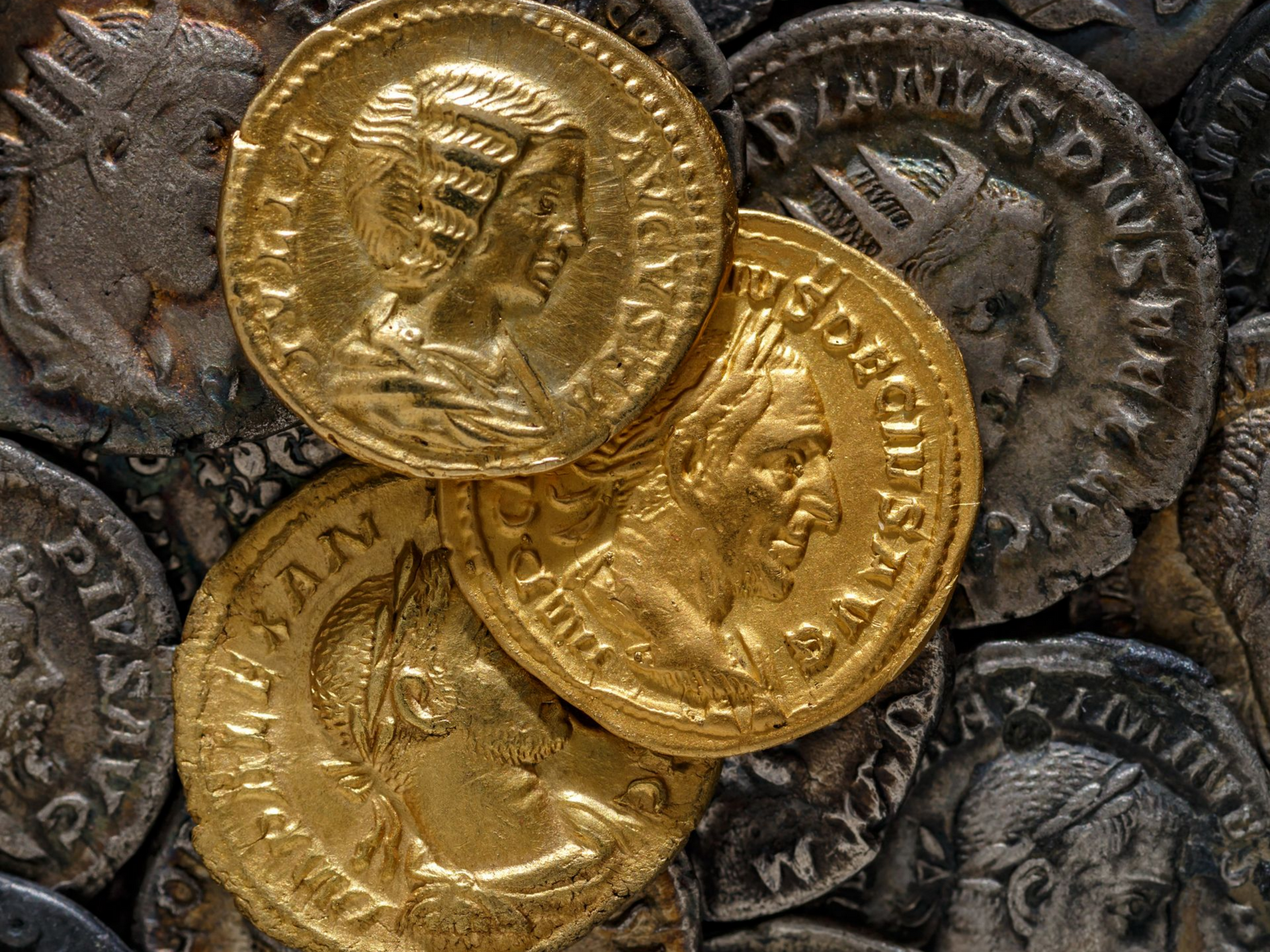 Gros plan sur des pièces romaines d'or et d'argent. On y voit des profils d'empereurs, des inscriptions latines et différents degrés de ternissement.