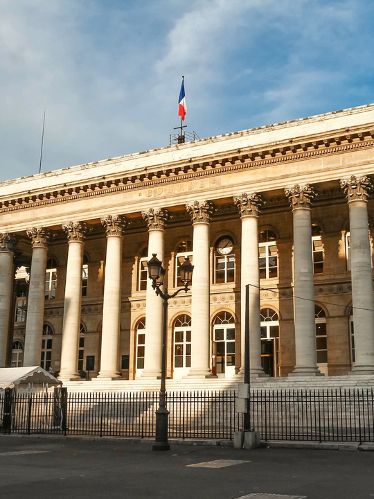 Bâtiment de la Bourse parisienne avec colonnes, drapeau français et lampadaire.