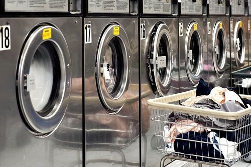 Una fila de lavadoras en una lavandería con una cesta llena de ropa.