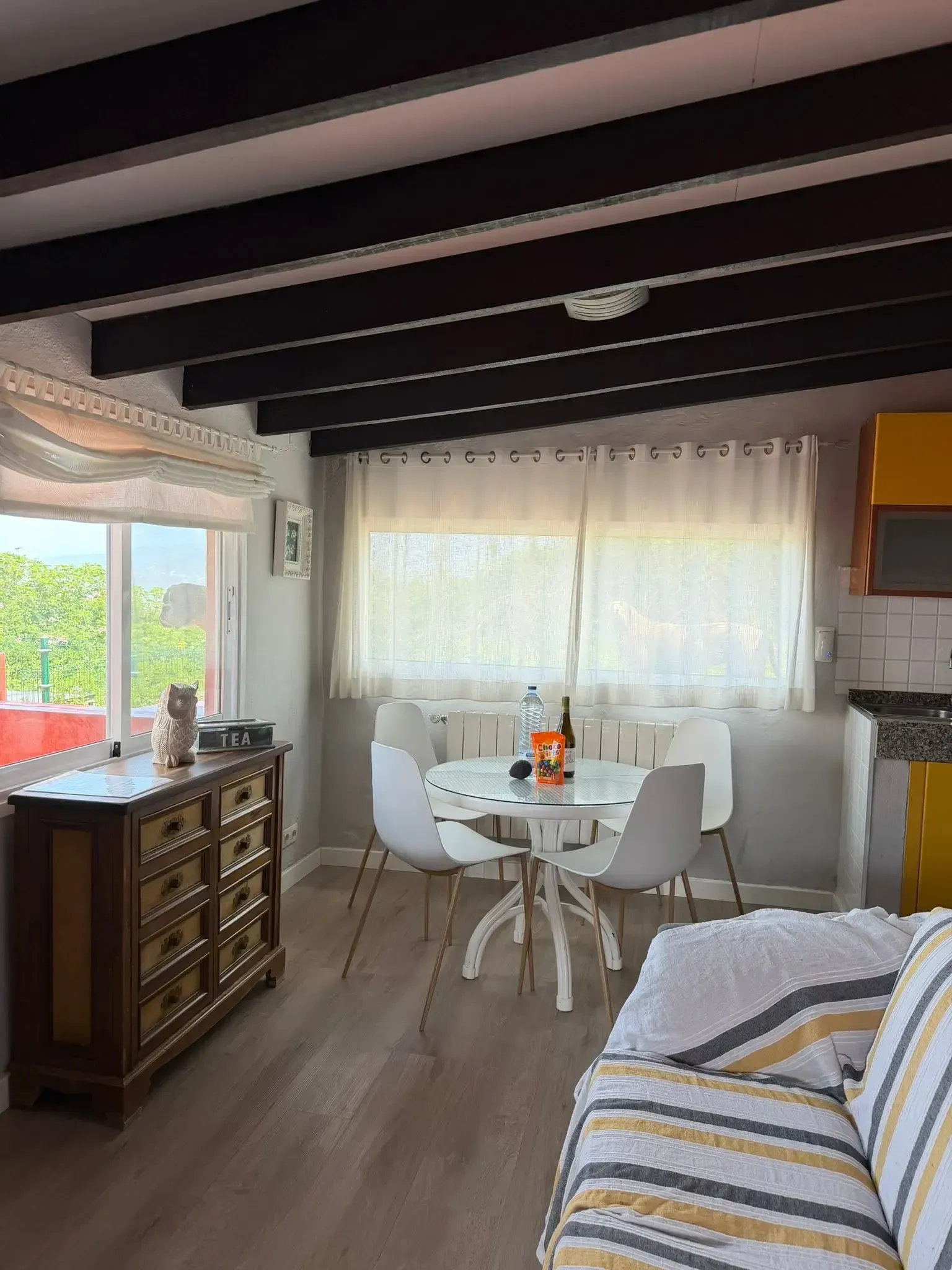 Una luminosa sala de estar con un aparador de madera, una mesa de comedor redonda con cuatro sillas blancas y un sofá a rayas.