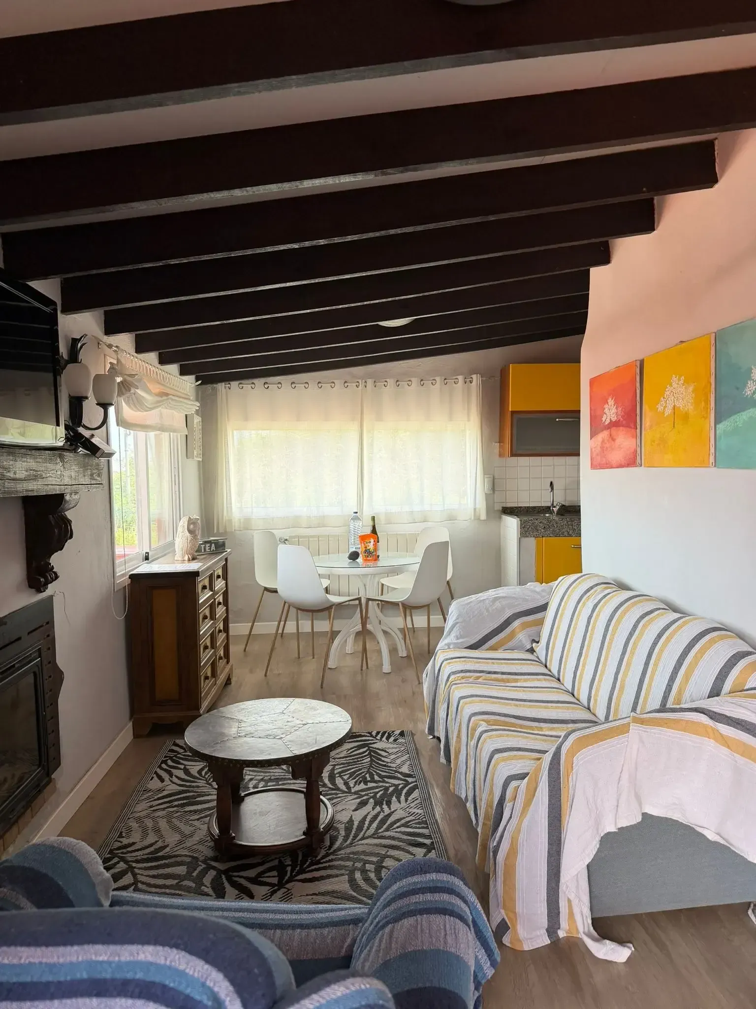 Una acogedora sala de estar con vigas de madera en el techo, una alfombra estampada, un sofá a rayas, una pequeña mesa de centro y un área de comedor.