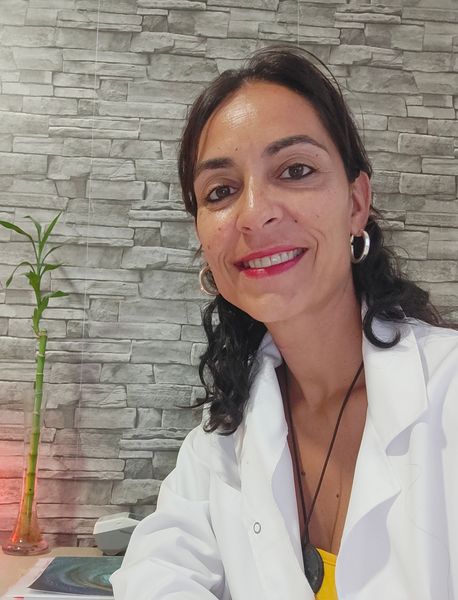 Una mujer con una bata blanca sonríe frente a una pared de ladrillos.