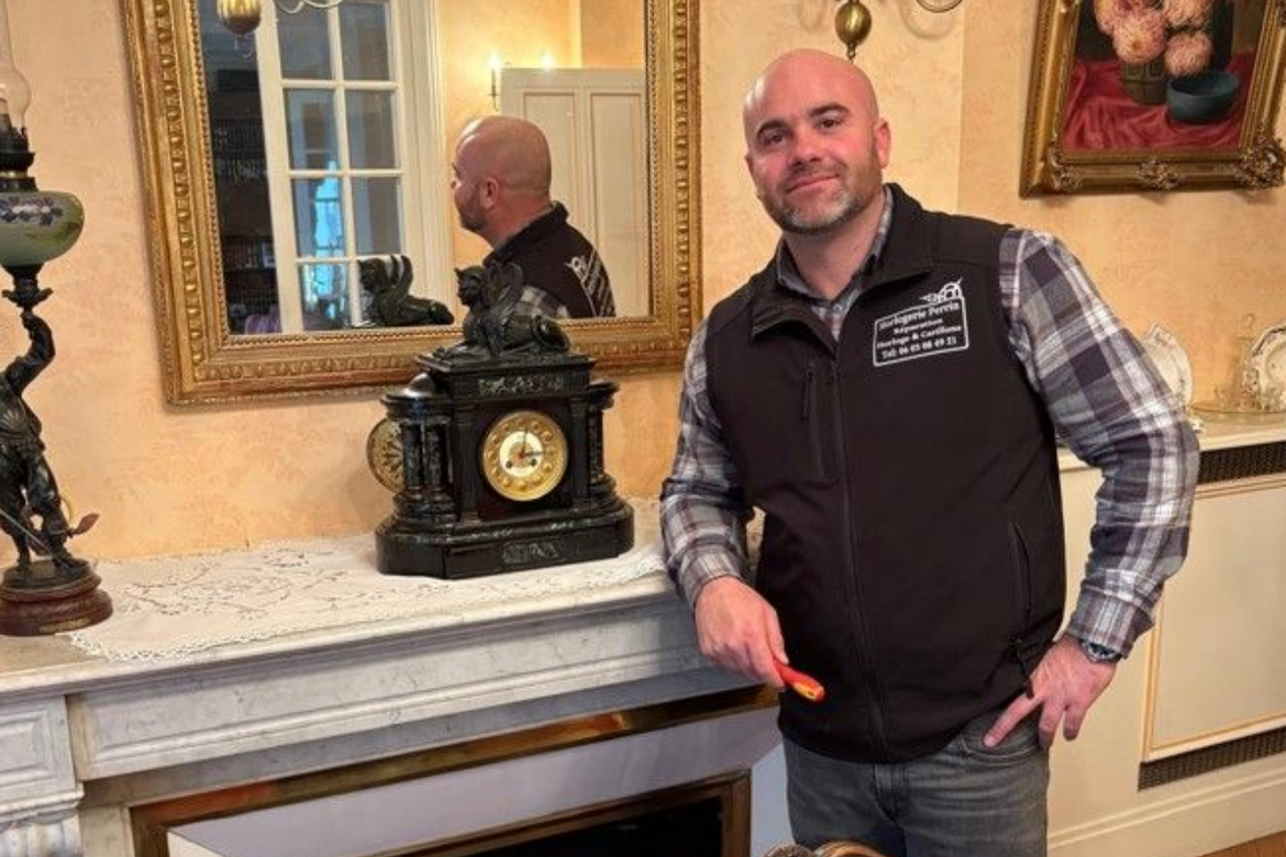 Un homme en gilet se tient près d'une cheminée où est posée une horloge.