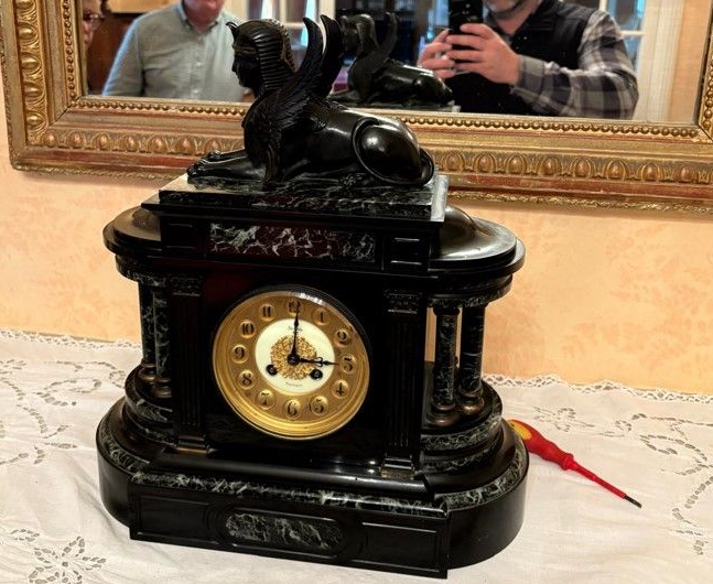 Horloge en marbre noir surmontée d'un sphinx, cadran doré, détails ornementés.