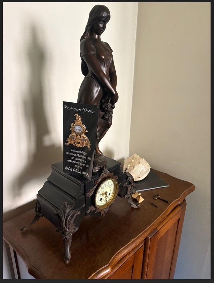 Une horloge ancienne ornée d'une statue en bronze représentant une femme repose sur un meuble en bois.