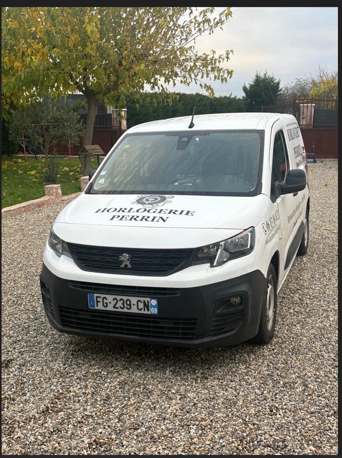 Fourgonnette Peugeot blanche avec logo de l'entreprise garée sur une allée de gravier.
