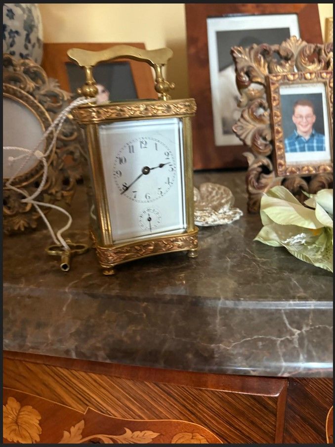 Une horloge dorée sur une table, avec une photo et d'autres éléments de décoration en arrière-plan.
