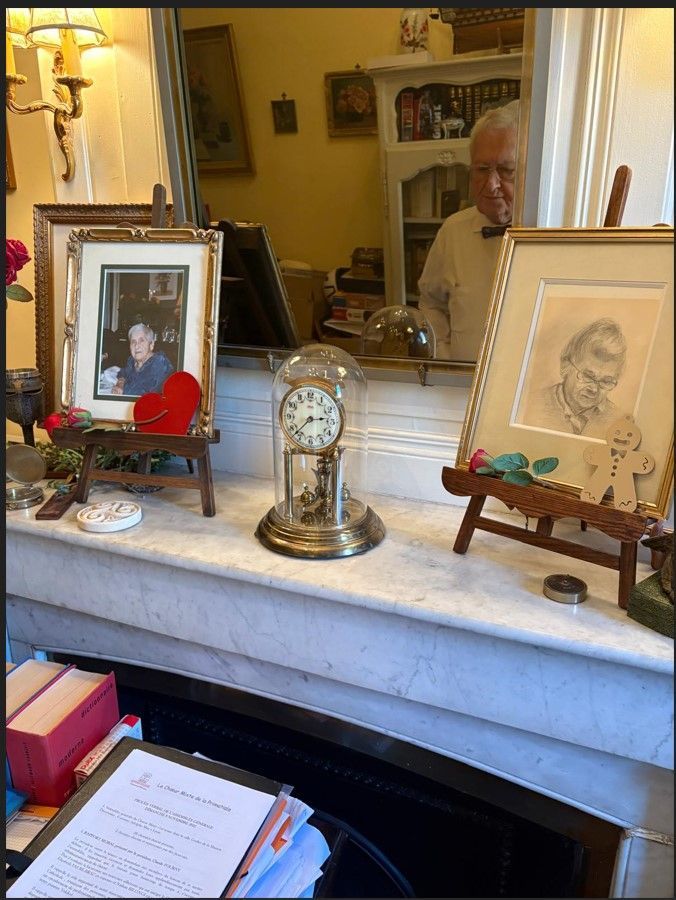 Cheminée ornée de portraits, d'une horloge et d'une rose.