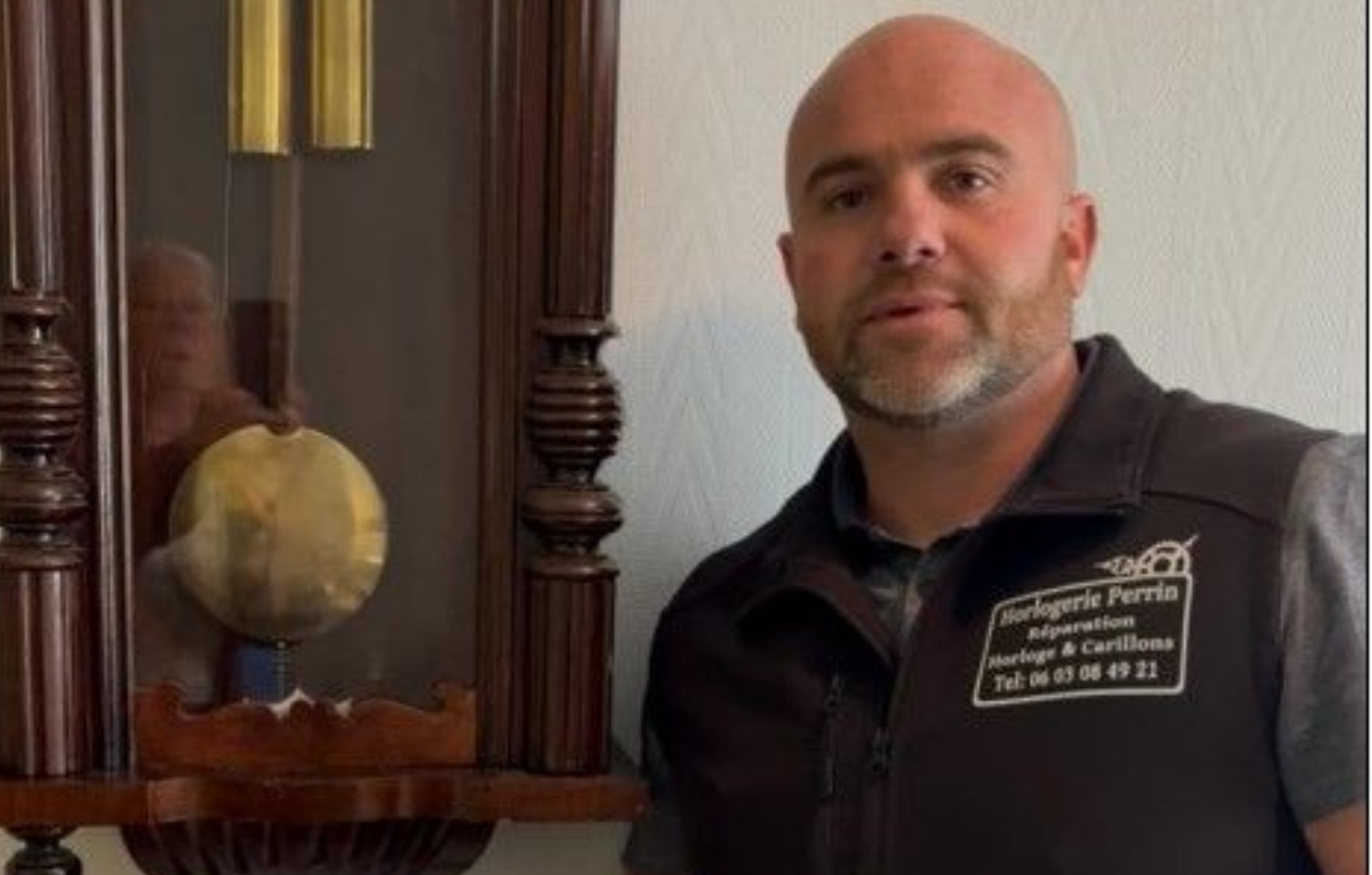 Un homme en gilet noir se tient à côté d'une horloge murale.