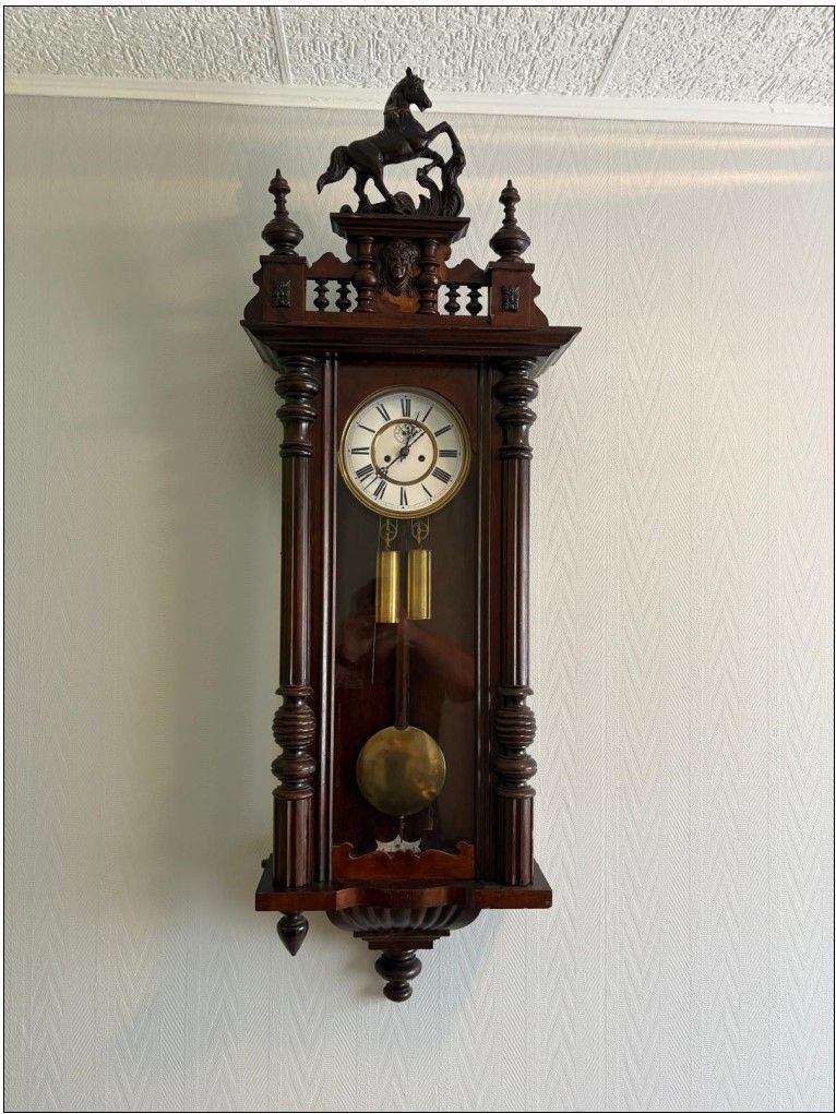 Horloge murale avec cadre en bois foncé, figurine de cheval sur le dessus et pendule.