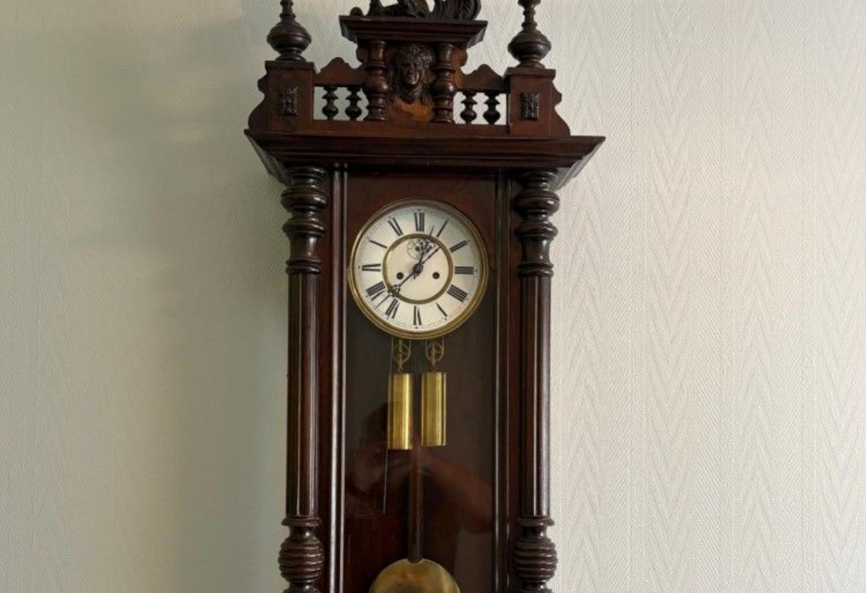 Horloge murale ancienne en bois, ornée de sculptures et dotée d'un pendule.