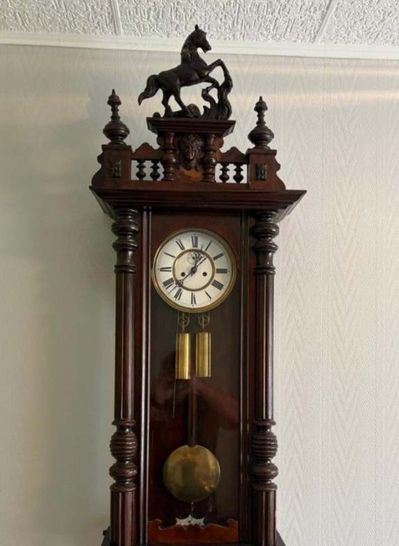 Horloge murale en bois surmontée d'une sculpture de cheval.