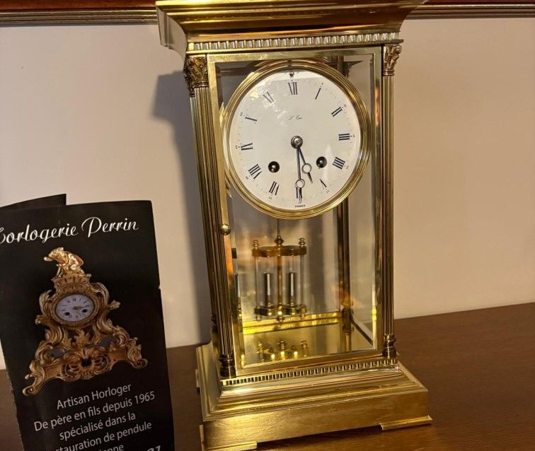 Pendule dorée avec panneaux de verre, laissant apparaître le cadran et le pendule.
