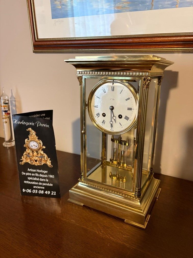 Une horloge ancienne à cadre doré est posée sur une table en bois.