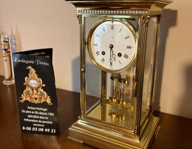 Horloge ancienne à cadre doré et cadran blanc, posée sur une surface en bois.