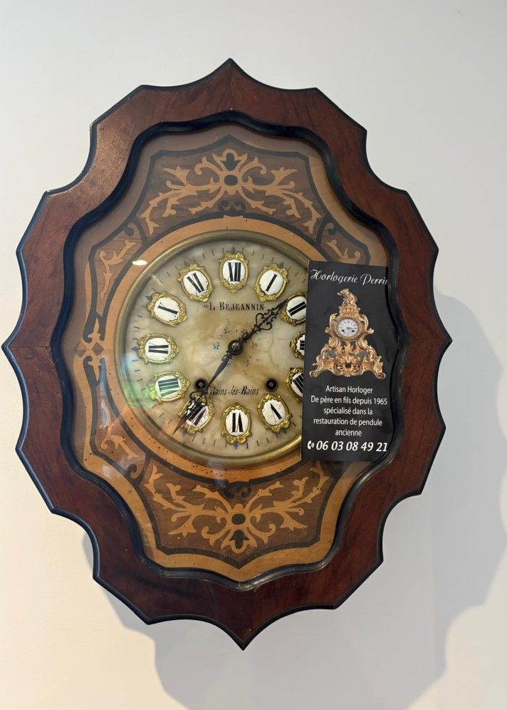 Horloge ancienne en bois avec un motif floral autour du cadran et une carte de visite sur le côté droit.