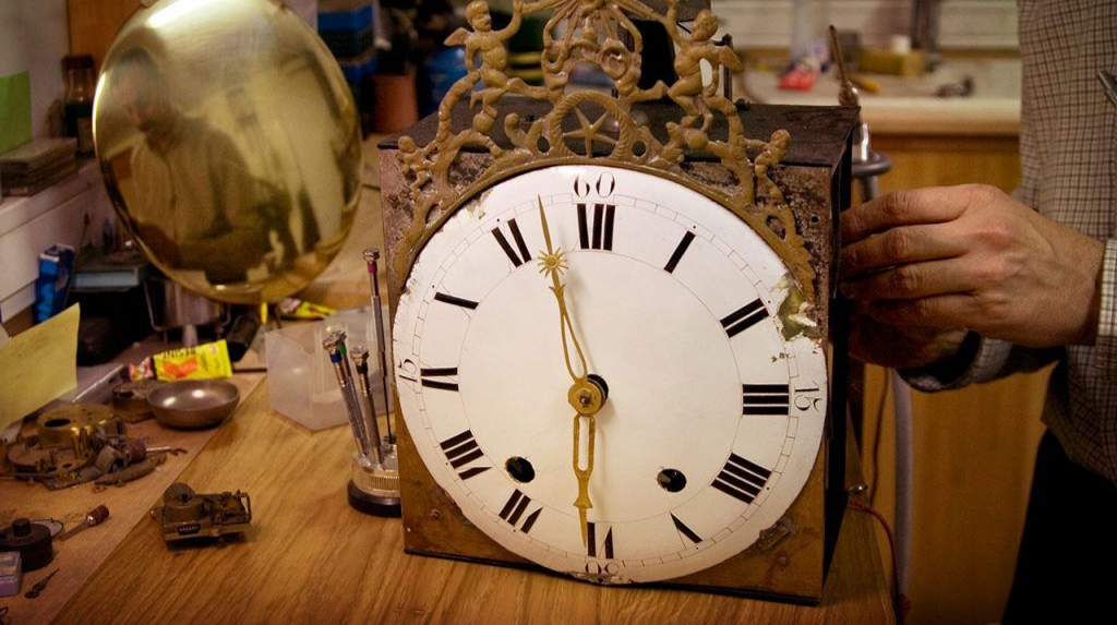 Un artisan ajuste les rouages d’une horloge dorée.