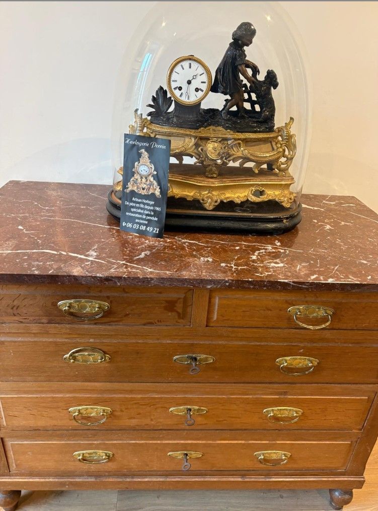Commode brune à plateau en marbre, horloge ornée sous un dôme de verre.