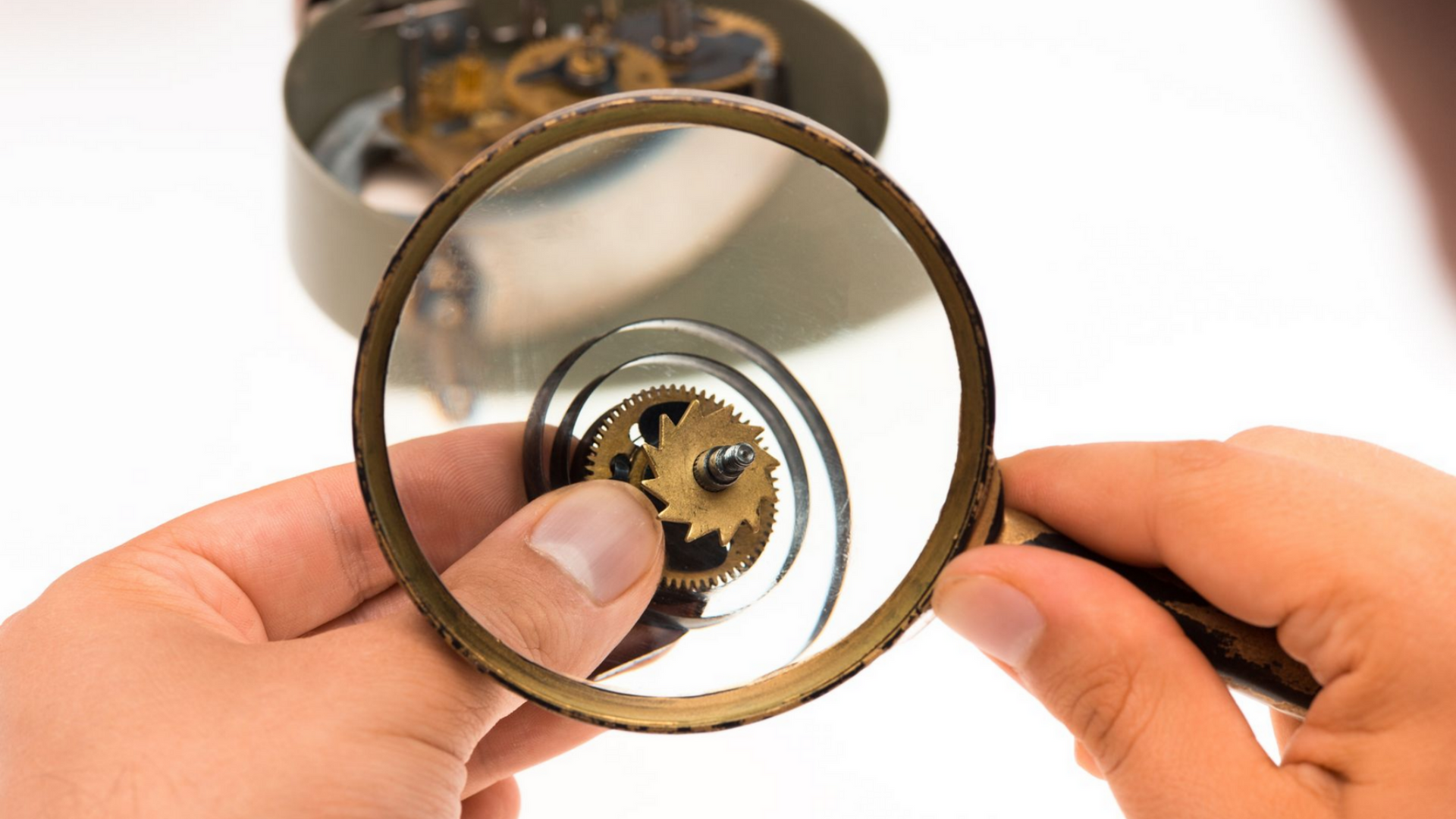 Mains examinant les engrenages d'une horloge avec une loupe.
