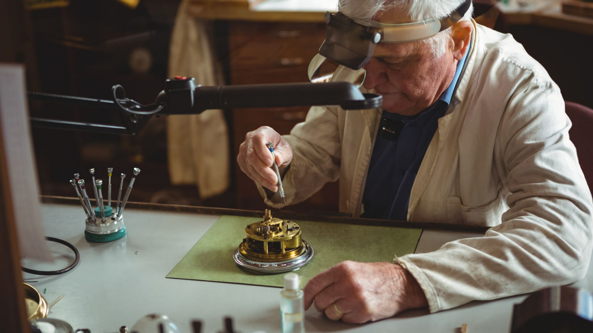 Un horloger expérimenté en blouse blanche utilise des outils sur un mécanisme d'horloge, en se concentrant intensément.
