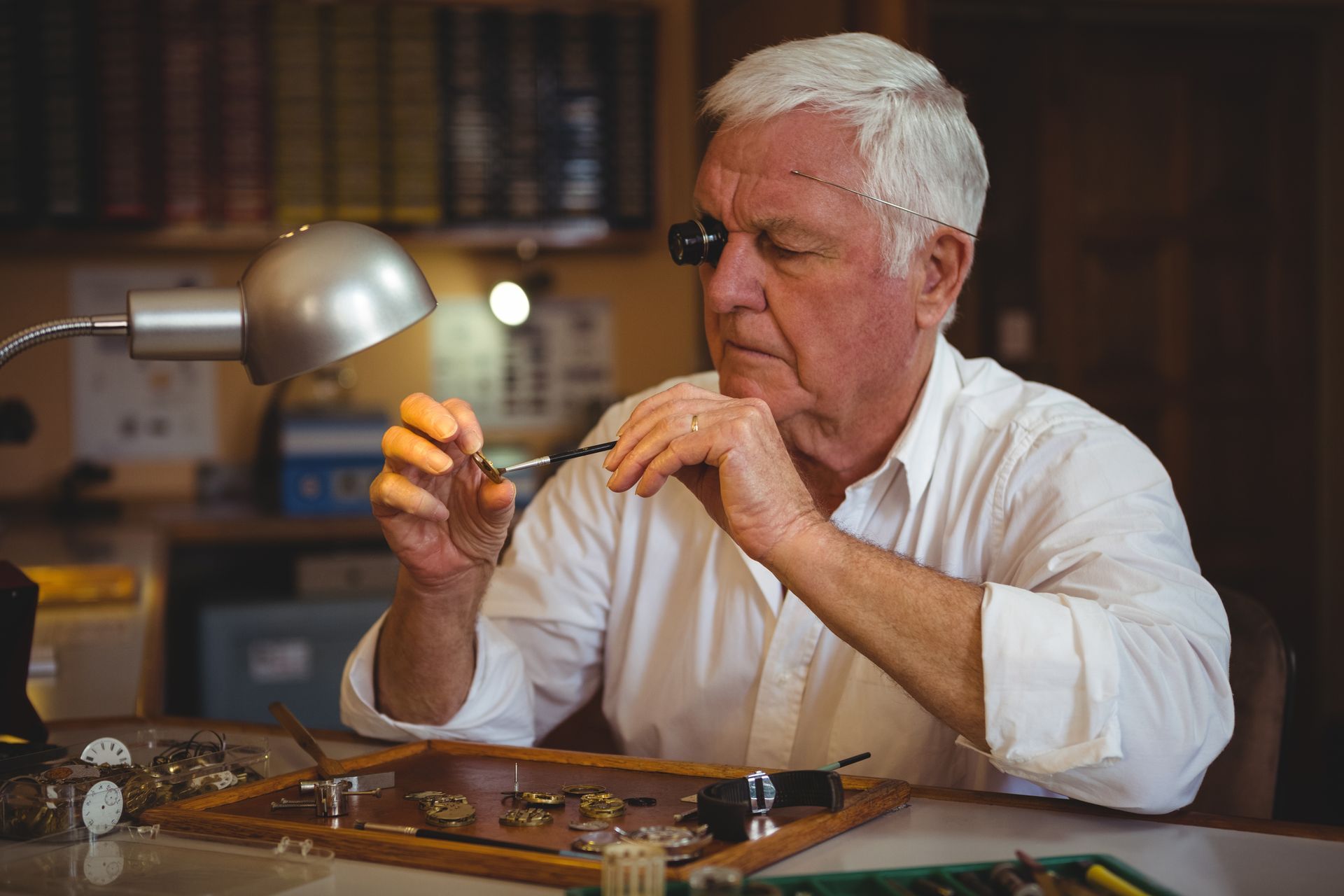 Horloger avec un oculaire grossissant travaillant méticuleusement sur des composants de montre sur un établi.