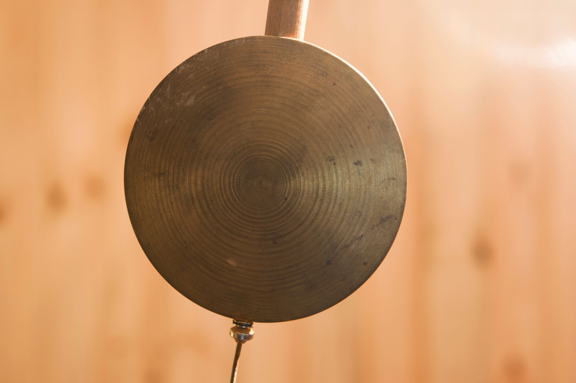 Pendule à disque en laiton, circulaire à anneaux concentriques, suspendue sur un fond en bois.