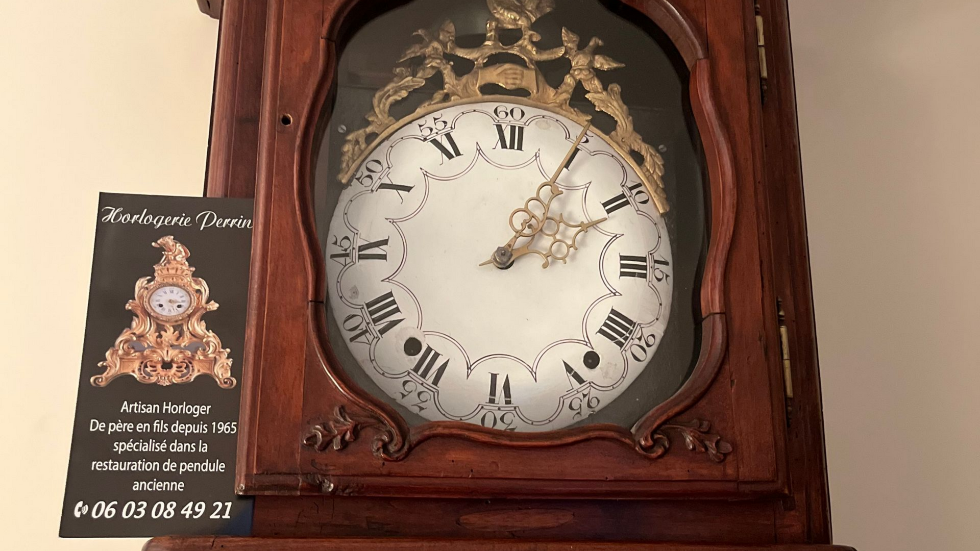 Horloge grand-père ancienne en bois avec cadran blanc, détails dorés et carte noire.