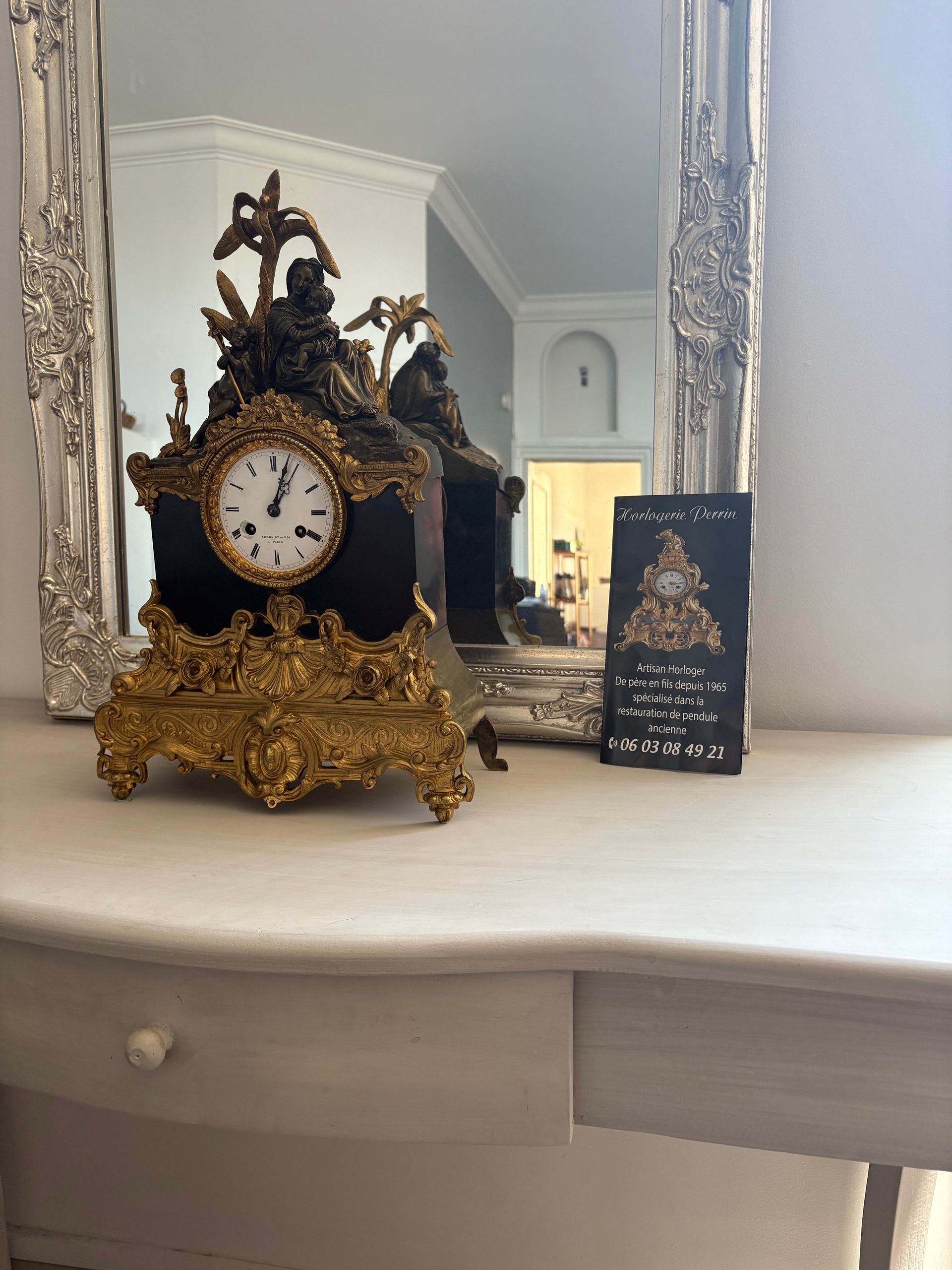 Pendule noire et dorée posée devant un miroir.
