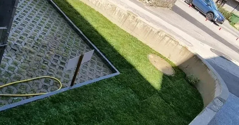 Prato verde accanto a un marciapiede in cemento e a un parcheggio con un'auto blu parcheggiata.