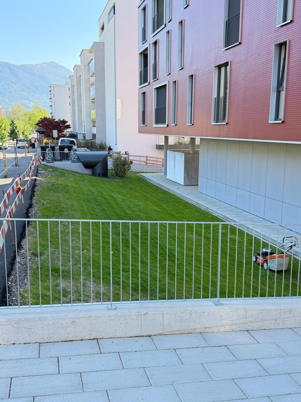 Prato verde accanto a un marciapiede in cemento e a un parcheggio con un'auto blu parcheggiata.