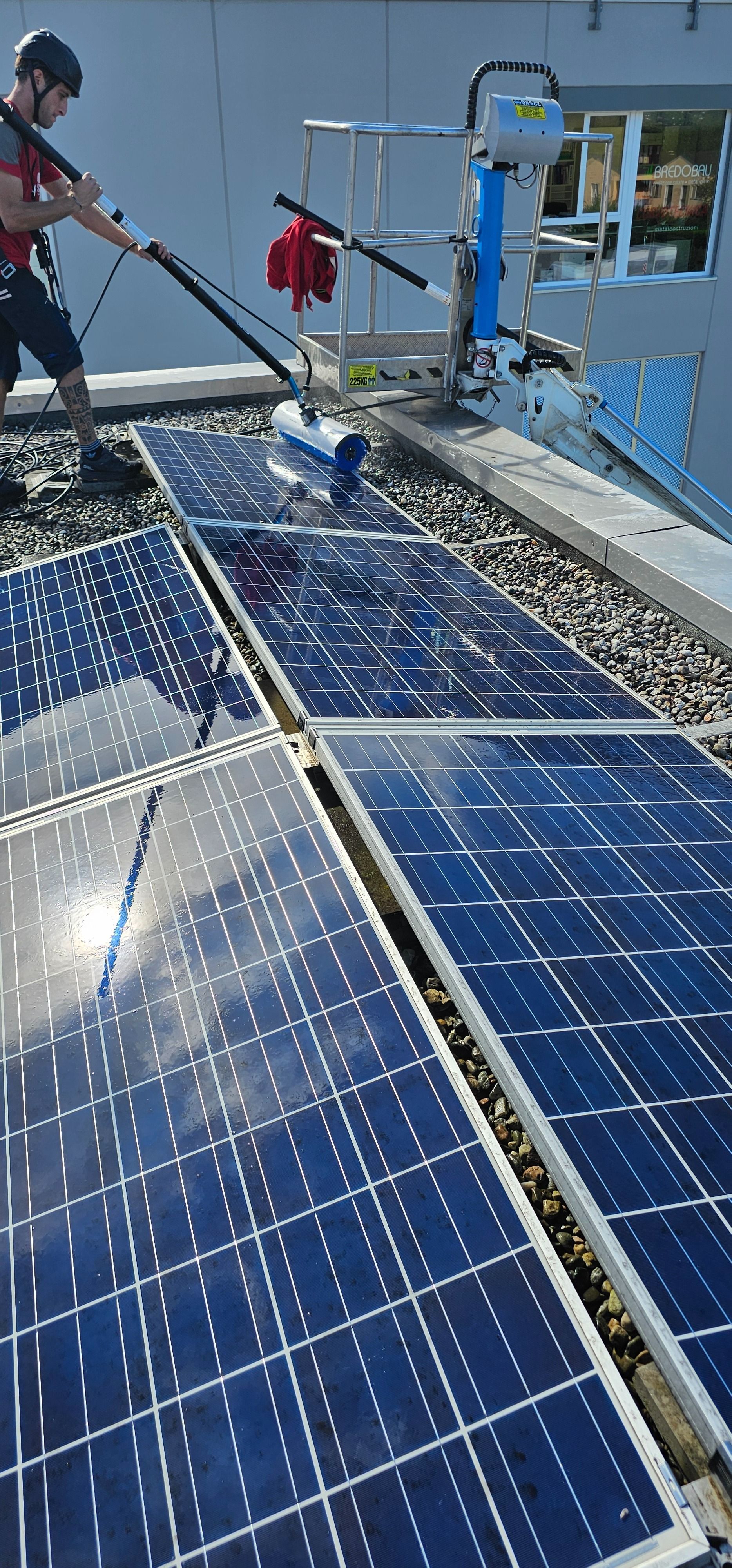 Persona che pulisce i pannelli solari con un panno arancione su un tetto.