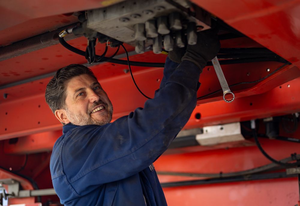 Ein Mechaniker untersucht ein Auto auf einer Hebebühne in einer Autowerkstatt und benutzt dabei ein Werkzeug unter dem Fahrzeug.
